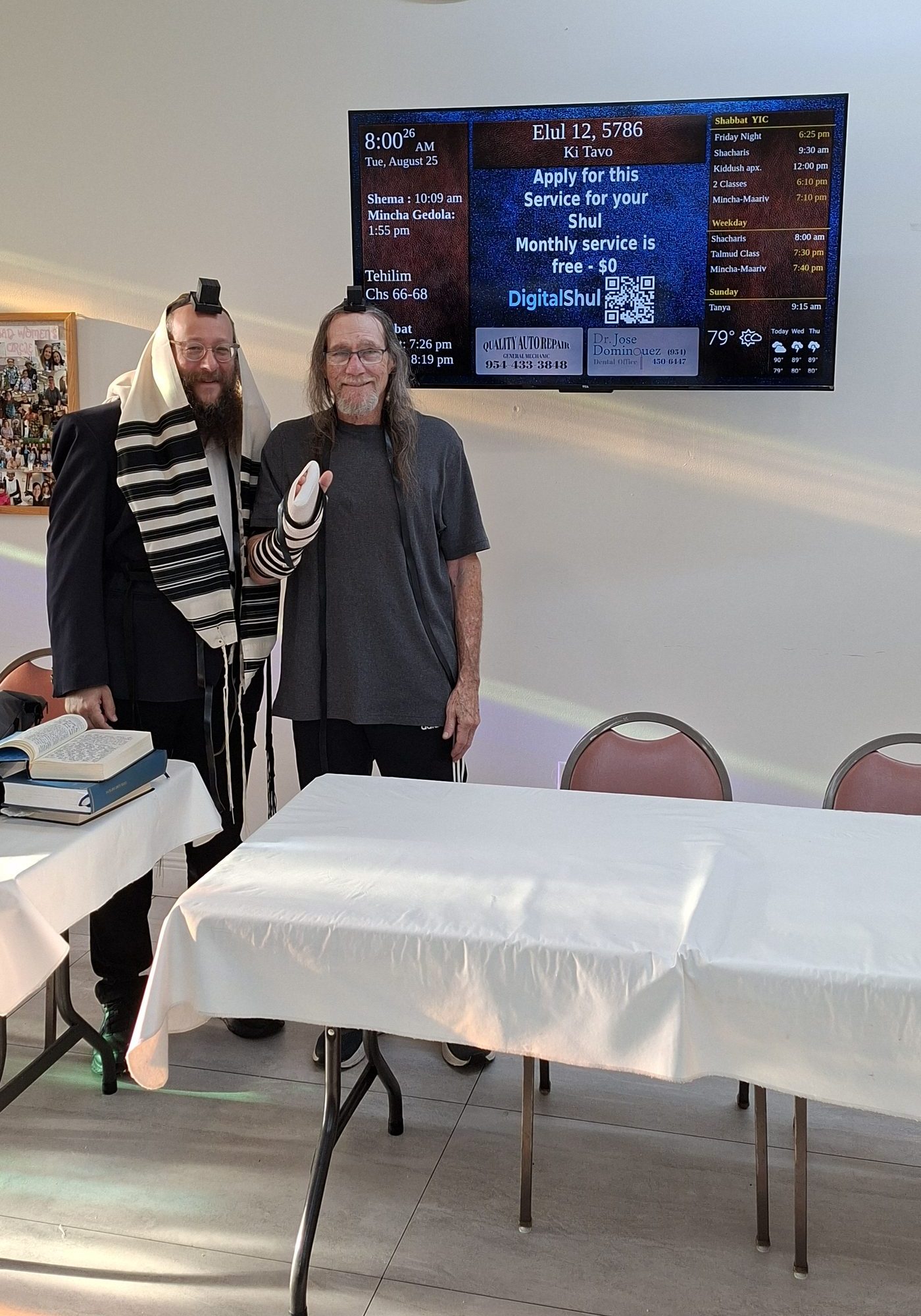 Rabbi and congregant in tallit and tefillin in front of the DigitalShul zmanim display