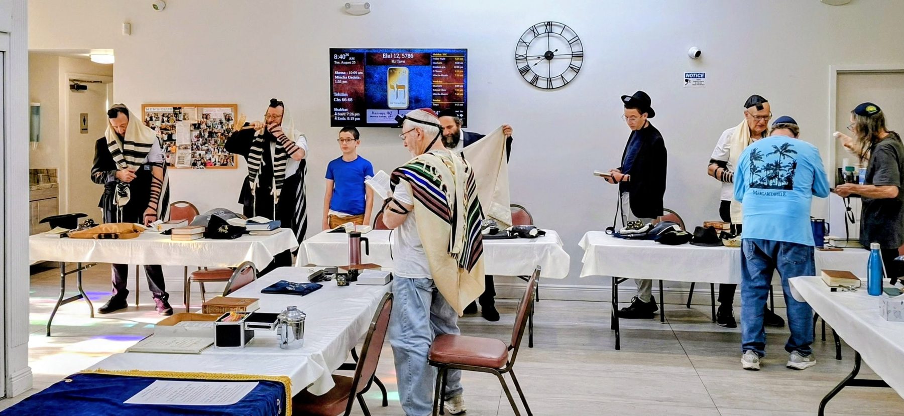 Weekday minyan in a synagogue with the zmanim display on the wall